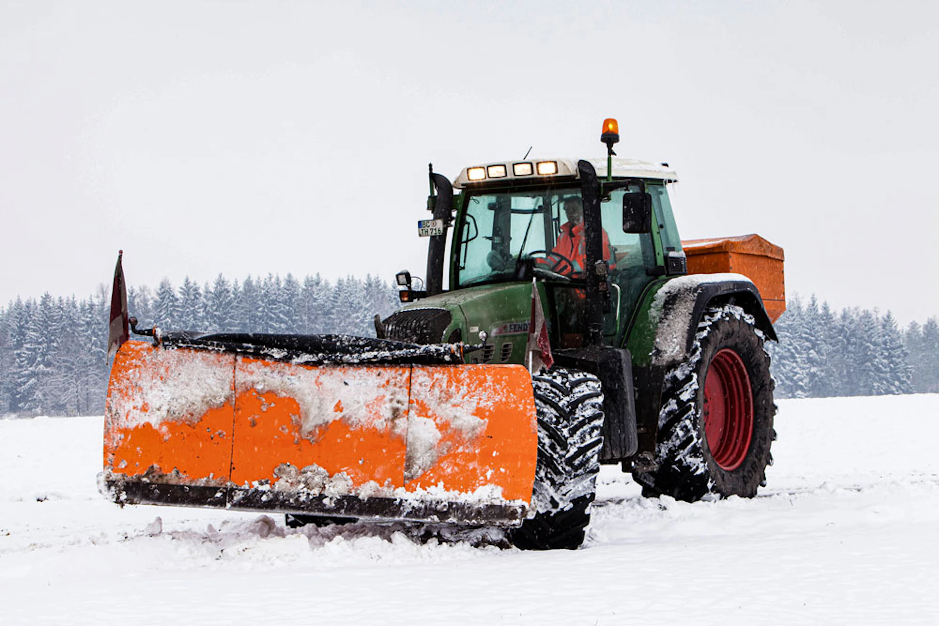 Traktor steht auf einer beschneiten Straße vorne dran hat eine große Schneschaufel dran
