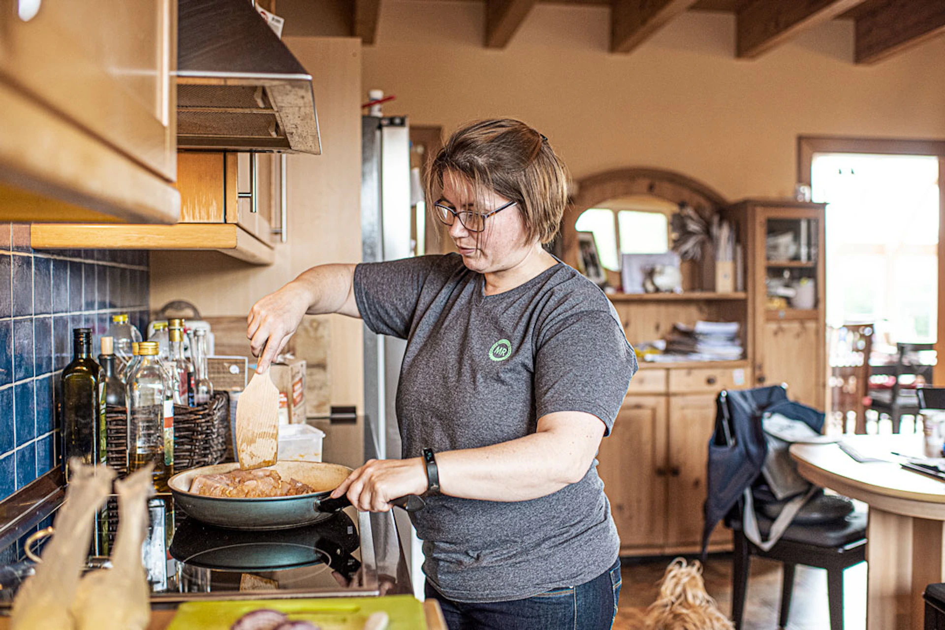 Frau steh in der Küche und bereitet mit einer Pfanne das Essen zu.