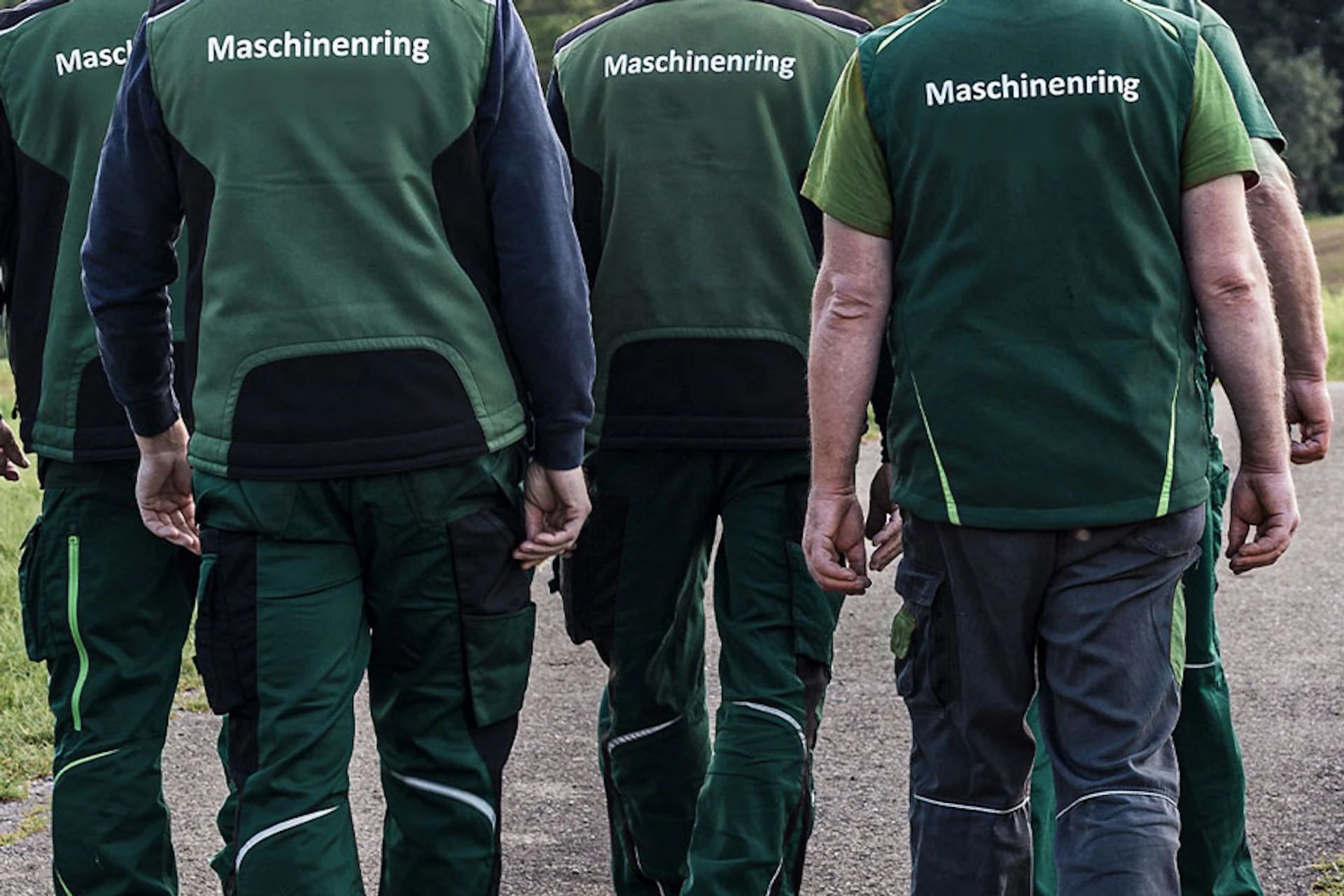 Fünf Männer laufen auf einer Straße, sie tragen grüne Westen, auf dem Rücken steht Maschinenring