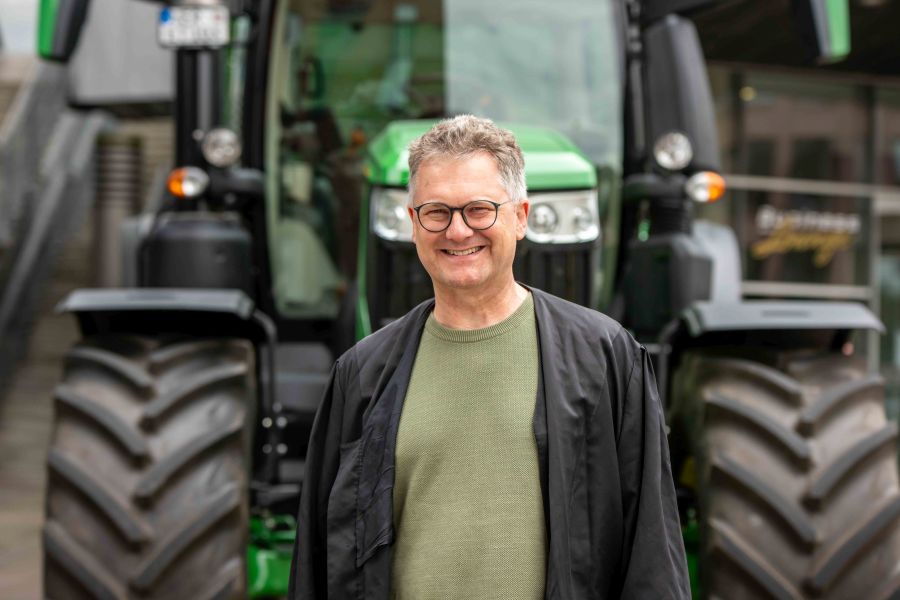 Dr. Christian Halm steht lächelnd vor einem großen, grünen Traktor. 