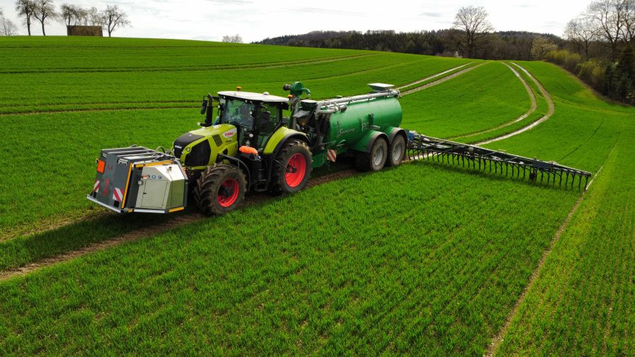 Ein Traktor mit Güllefass und Fronttank fährt über ein Feld.